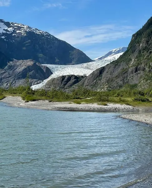 Scenic view of a glacier nestled between mountains under a clear blue sky, with a tranquil lake in the foreground.
