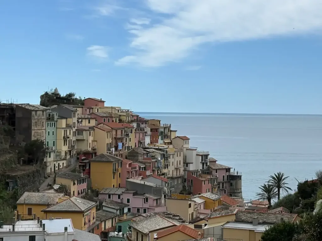 Colorful coastal village buildings overlook the serene sea under a bright blue sky.