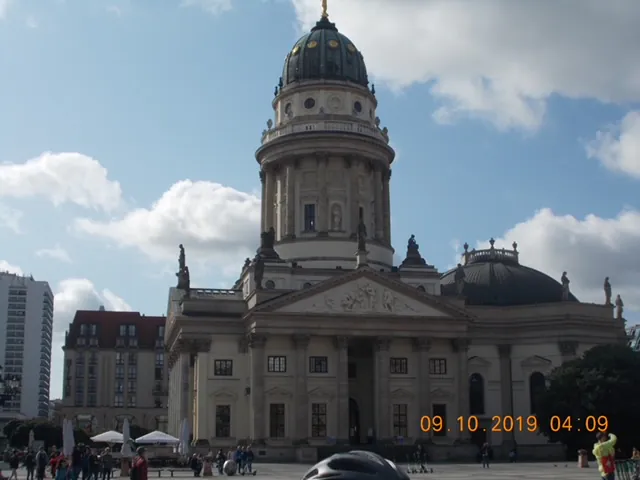 Historic building under a blue sky with clouds, featuring a large dome and classic architectural details.