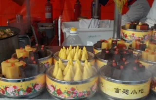 Assorted colorful steamed buns and cakes displayed in metal trays at a street food stall.