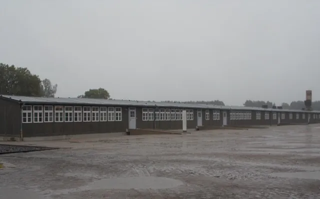 Overcast skies above a long, empty industrial building with multiple windows and a wet concrete ground.