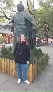 Woman in front of a large historical statue near a KFC in a park setting, surrounded by greenery.
