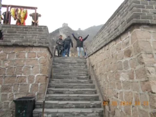 Two people standing on stone steps at the Great Wall of China, one with arms raised, on a foggy day.