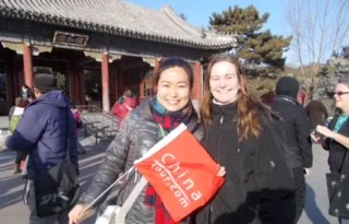 Two tourists smiling and holding a China tour sign in front of a traditional Chinese building.