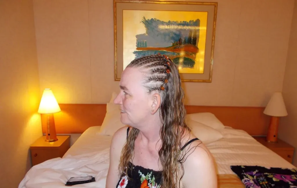 Woman with braided hairstyle sitting on a bed in a well-lit hotel room with colorful wall art.