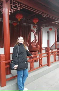 Person in a coat standing by a large decorative teapot sculpture in a traditional Chinese setting.
