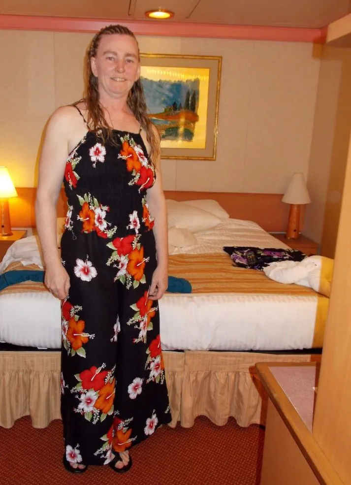 Woman in a floral black dress stands in a cozy hotel room with a bed and warm lighting.
