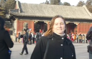 A tourist poses in front of a traditional Chinese building, surrounded by visitors on a clear day.