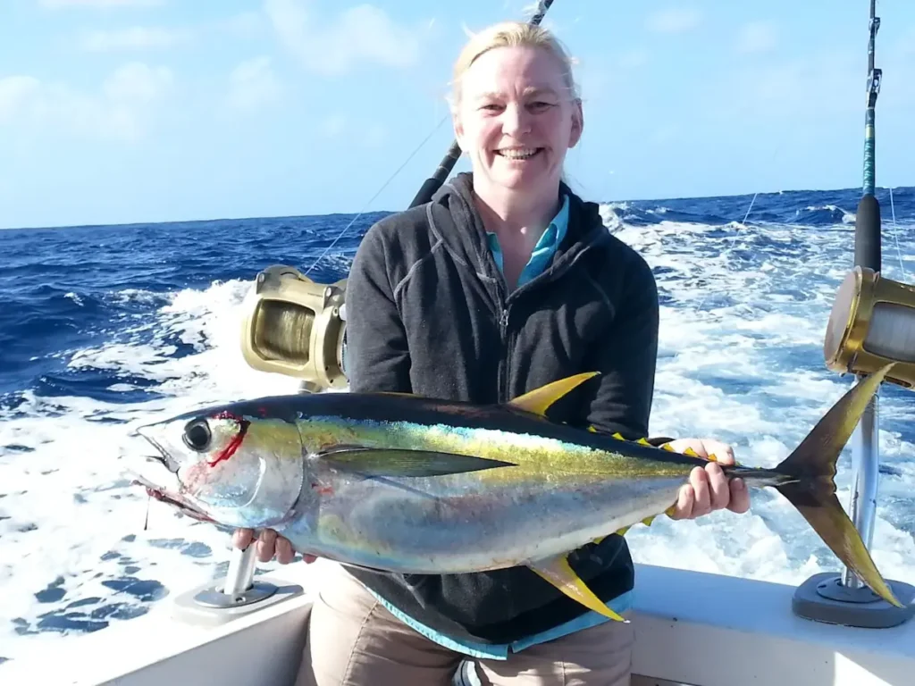 Smiling person holding a large tuna on a boat with ocean waves in the background.