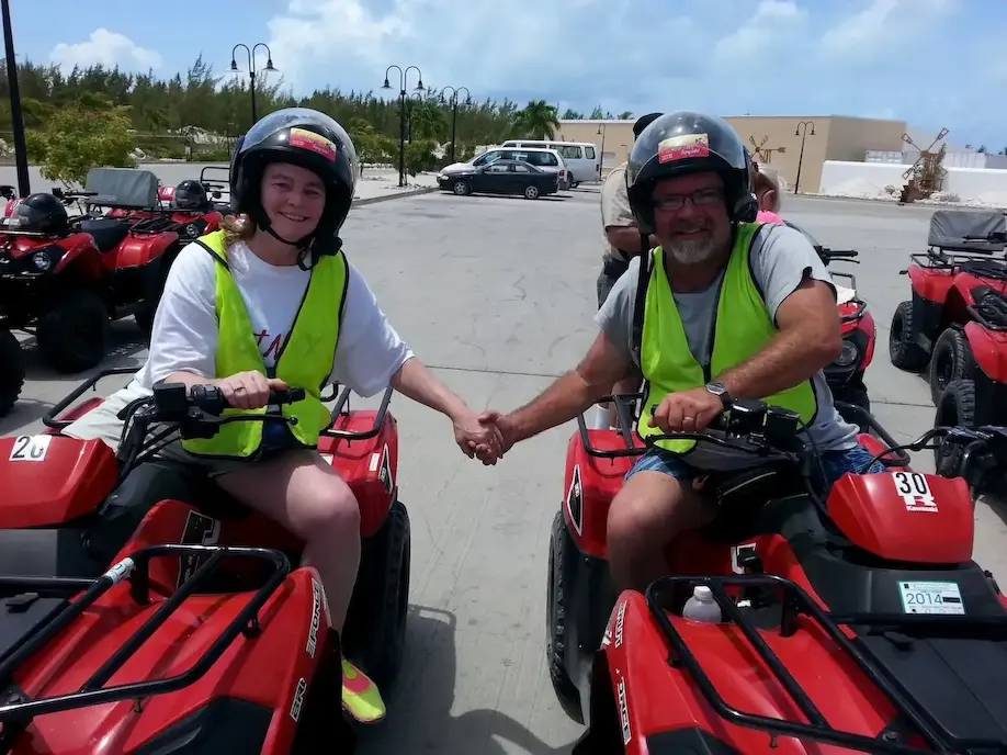 Two people wearing helmets and vests holding hands on red ATVs, ready for an outdoor adventure.