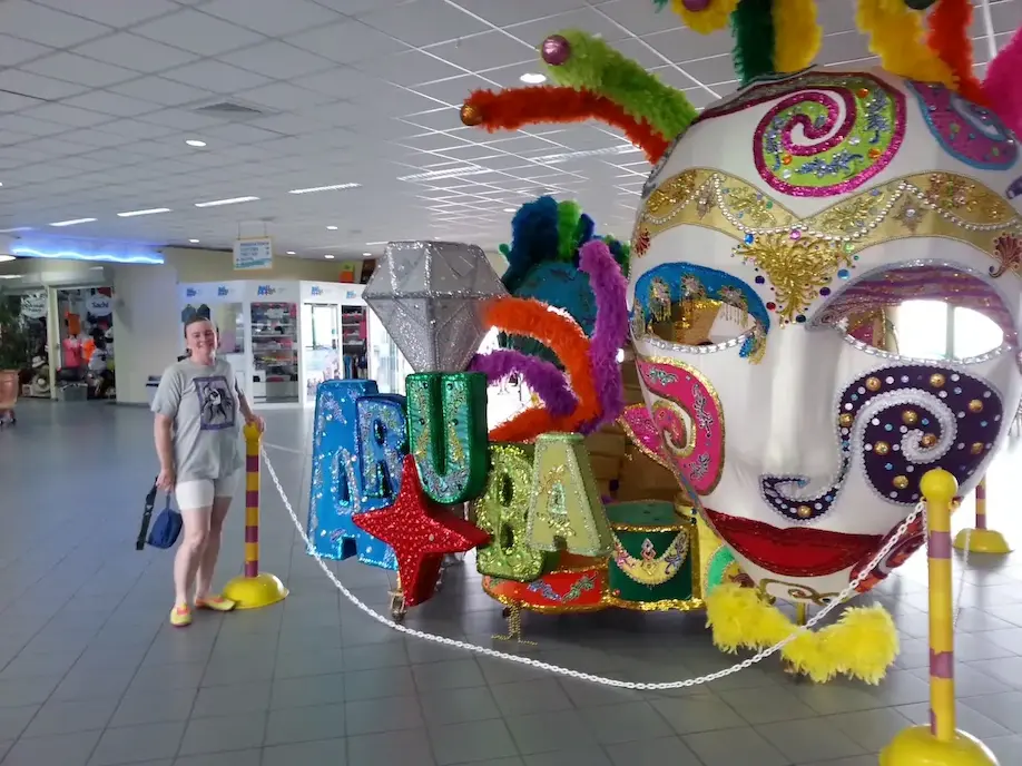 Colorful Aruba carnival mask display in a bright room with a person standing nearby.