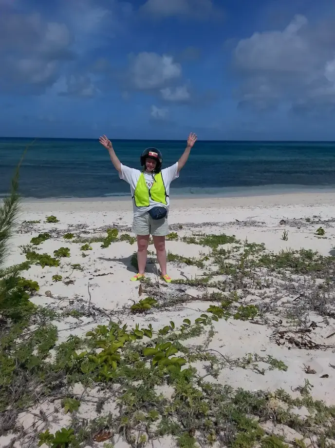 Person celebrating on a sandy beach with ocean waves and a blue sky in the background.