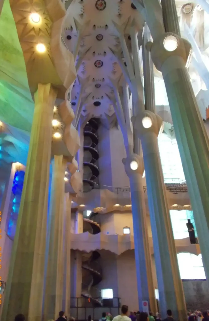 Interior of Sagrada Familia, showcasing ceiling details and columns with colorful light reflections.