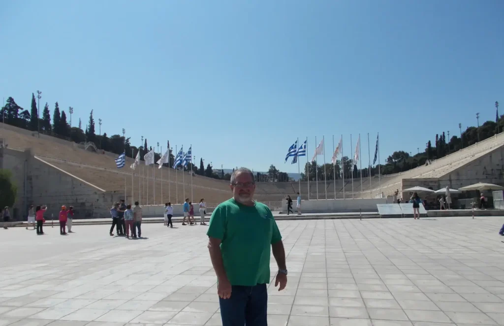 Visitor at the historic Panathenaic Stadium in Athens, Greece, with flags and stone seating in the background.