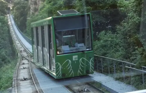Green funicular railway car ascending a forested mountain tramway.