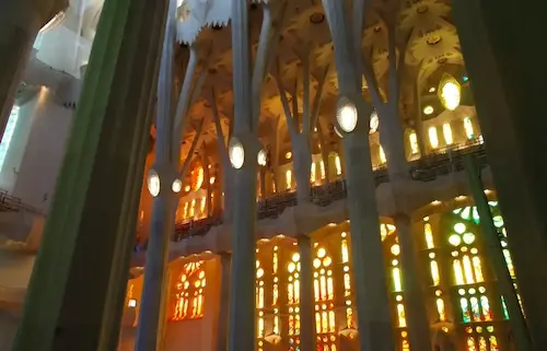 Interior of Sagrada Familia with colorful stained glass windows casting vibrant light through the grand columns.