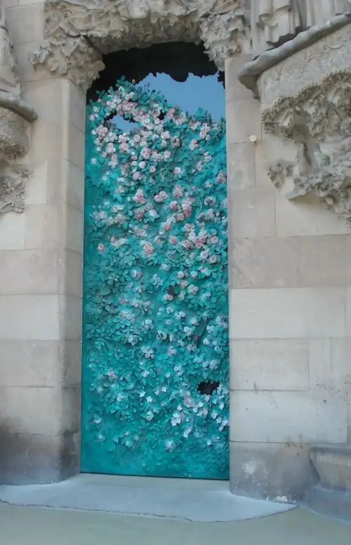 Ornate turquoise door covered with intricate floral design, set in a textured stone wall.